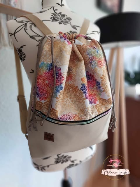 Cream canvas backpack with colorful floral patterned fabric pocket, displayed on a dress form with botanical print