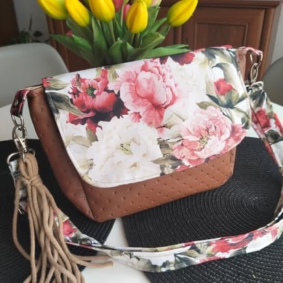 Floral handbag with brown leather trim and tassel strap on white chair with yellow tulips in background