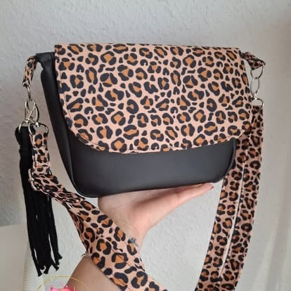 Leopard print shoulder bag with black leather flap and tassel strap held in hand