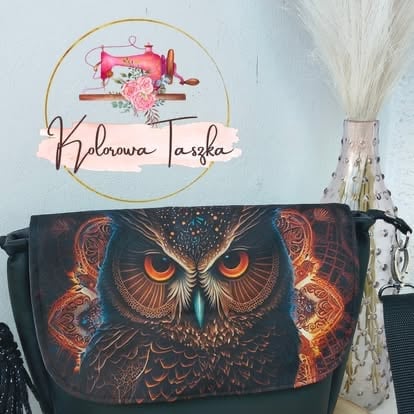 Black tote bag with fiery owl design displayed below a gold circular sign reading Kalinowa Laska with sewing machine logo