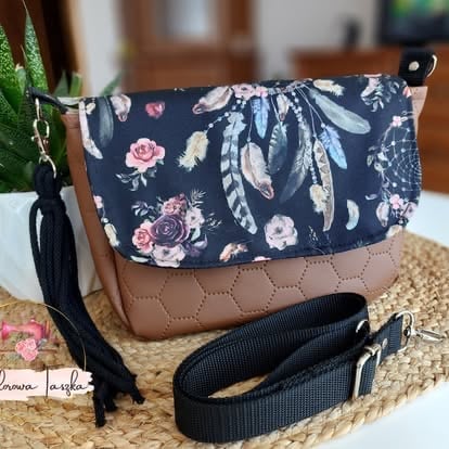 Navy floral crossbody bag with tan quilted leather bottom and black shoulder strap displayed on natural woven mat