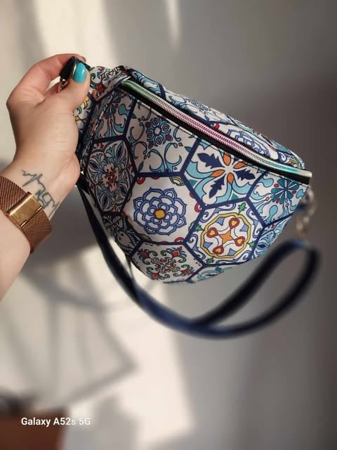 Person holding a blue and white patterned fanny pack with ornate tile designs and a black shoulder strap