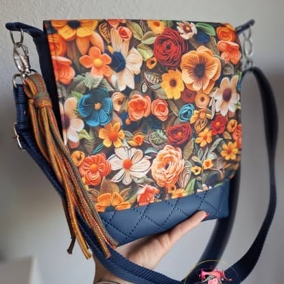 Floral crossbody bag with colorful flowers on dark fabric, navy blue bottom section, and tan tassel charm held in hand