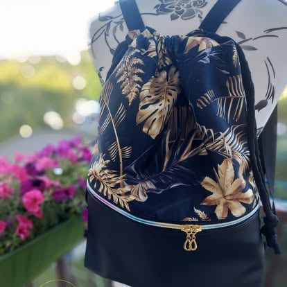 Dark navy drawstring backpack with gold botanical leaf pattern, worn outdoors near pink flowers and green grass