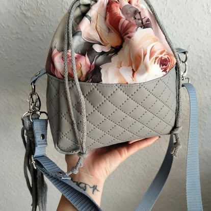 Hand holding a quilted beige crossbody bag with pink and coral flowers spilling out of the top